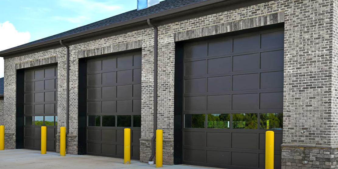 Team of commercial garage door repair specialists fixing a large industrial garage door on a commercial building, showcasing professional tools and safety gear for efficient service