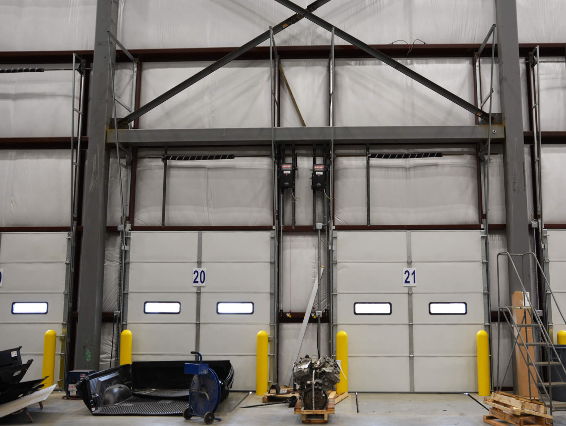 Technician performing commercial garage door repair on a large aluminum door at a business facility