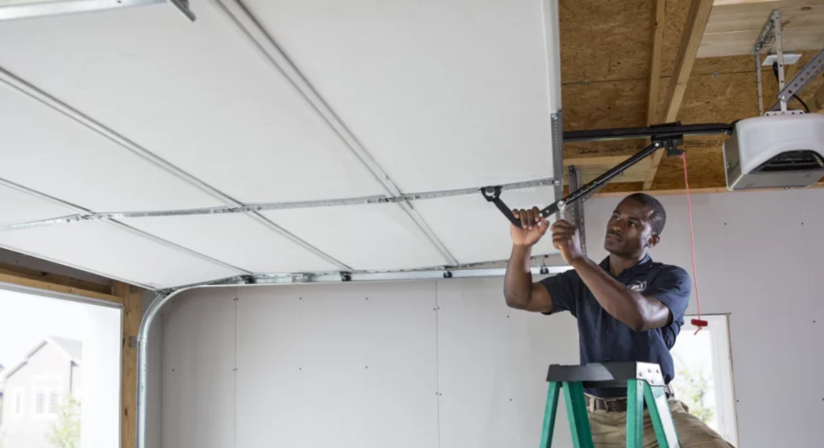Technician performing overhead garage door repair on a residential garage, using professional tools to adjust door mechanisms.